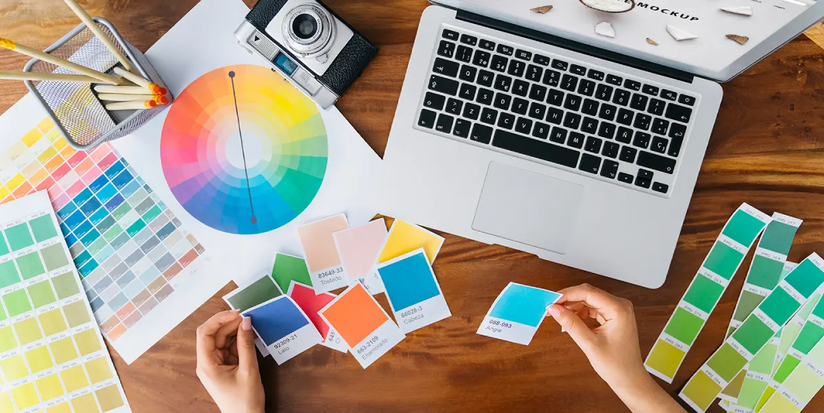 Mesa de trabajo con paletas de colores, círculo cromático y laptop, representando el proceso creativo de diseño gráfico y selección de identidad visual.